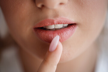 Obraz premium The bride girl with large magnificent lips and healthy white teeth presses a finger with a long manicure to her mouth. Very close-up, macro shot