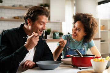 Boyfriend and girlfriend eating lunch together at home. Husband and wife enjoying in delicious food.