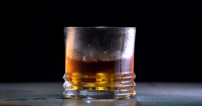 Bartender Throws ice and Whiskey poured into a glass with ice on a gray wooden table background. front view. Black background. Alcohol concept