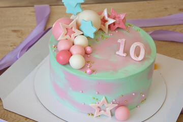 A beautiful birthday cake decorated with chocolate balls and pink and blue stars. With number 10 on a blue background. Place for an inscription.