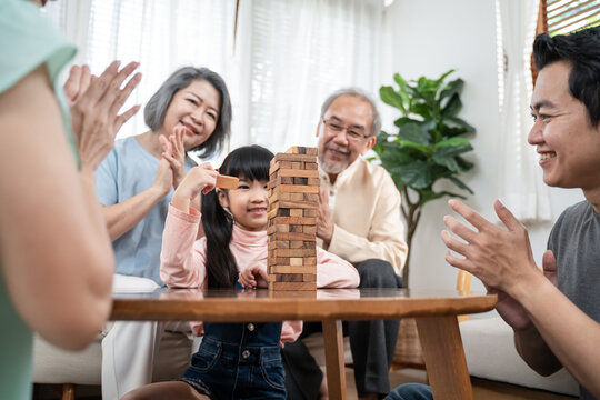 Asian Big Family Cheering Kid Playing Jenga Game In The Living Room.