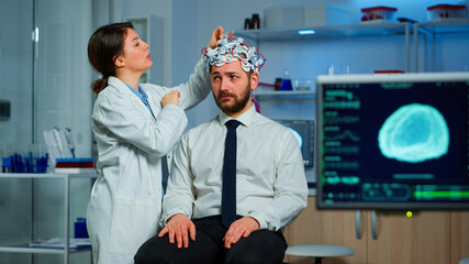 Patient with brain scan discussing with researcher neurological doctor while adjusting brainwave scanning headset examining diagnosis of disease, explaning eeg results, health status, brain functions