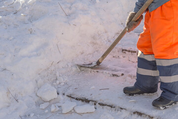 A worker clears the snow from the stairs in a city park on a sunny day. Selective focus.