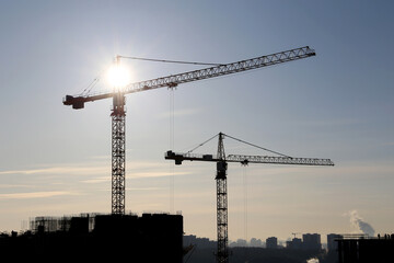 Tower cranes and construction site on sunshine background. Housing development, apartment block in city