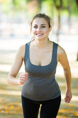 Young happy female in sportwear running in the sunny park.