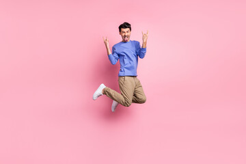 Fototapeta na wymiar Full body photo of crazy funny man jump up make hands horned signs stick out tongue isolated on pink color background