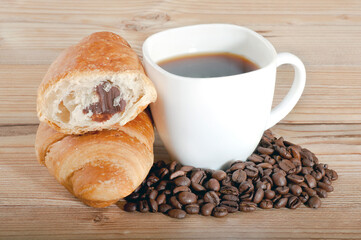 Croissant with coffee and beans on wooden background