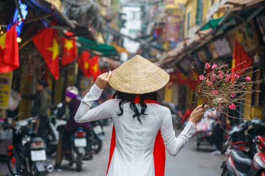 Vietnamese girl with traditional dress (ao dai) on Hanoi street with peach flower in hand during Tet holiday in Hanoi, Vietnam