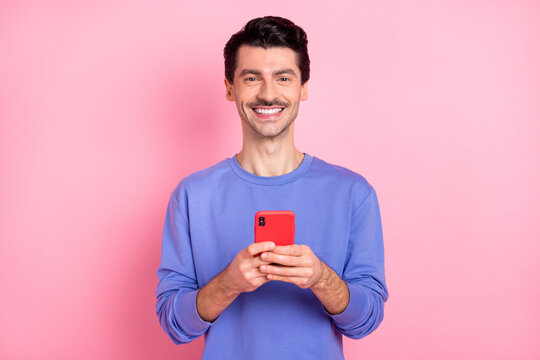 Photo of positive happy young guy hold phone good mood post comment isolated on pink color background