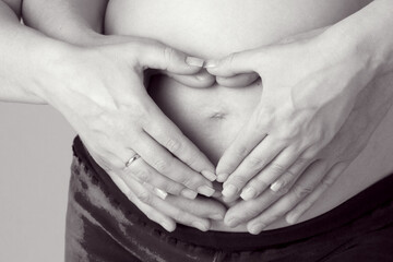 Male and female hands on a pregnant belly. The fingers are intertwined in the shape of a heart. Married couple hugs pregnant belly