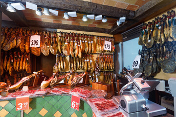 Fototapeta na wymiar Assortment of delicious Spanish meat shop with dangling legs jamon and packings of sliced ham