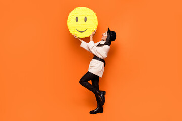 Fototapeta na wymiar Full size photo of young beautiful charming smiling girl hold huge yellow smile emoji isolated on orange color background