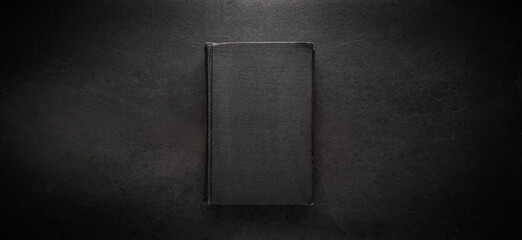 An old book with a black cover on a black metal background. The book is closed.