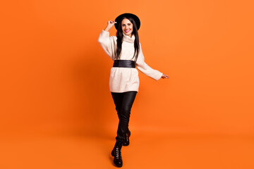 Full size photo of young smiling beautiful pretty woman dancing adjusting black hat isolated on orange color background