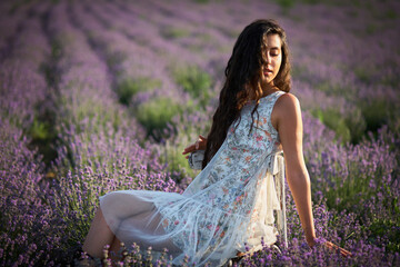Beautiful girl in a white sarafan sits on a wooden chair and poses in the middle of a lavender...