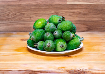 Green feijoa fruits in a white plate on a wooden background. Tropical fruit feijoa. Set of ripe feijoa fruits.