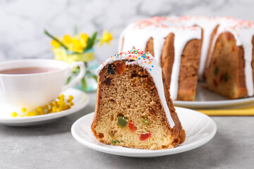 Piece of glazed Easter cake with sprinkles and candied fruits on grey table, closeup