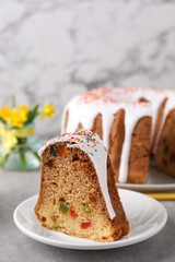 Piece of glazed Easter cake with sprinkles and candied fruits on grey table