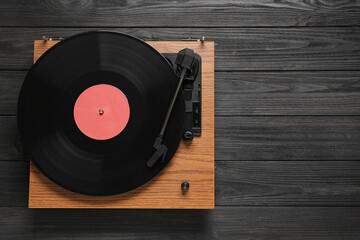 Turntable with vinyl record on black wooden background, top view. Space for text