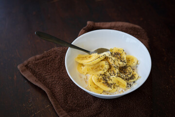 A close up of cereal bowl with sliced bananas sprinkled with chia seeds in a bowl on a dark background.