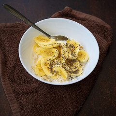 A close up of cereal bowl with sliced bananas sprinkled with chia seeds in a bowl on a dark background.
