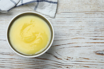 Bowl of Ghee butter on white wooden table, top view. Space for text