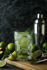 Glass of mojito cocktail and ingredients against dark smoky background