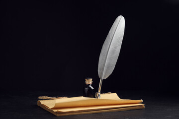 Feather pen, bottle of ink and old paper on black table