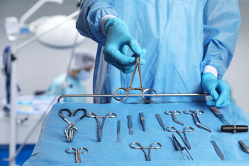 Nurse near table with different surgical instruments in operating room, closeup