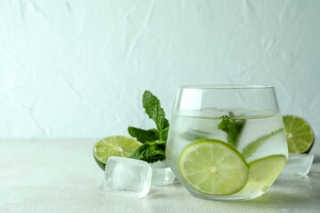 Glass of mojito cocktail and ingredients on white textured table