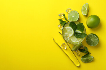 Glass of mojito cocktail and ingredients on yellow background