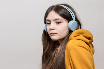 A sad teenage girl, 12-13 years old, sits in headphones sweatshirt on a white background copy space...