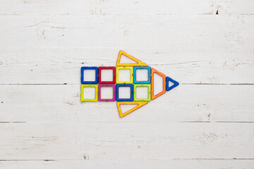 Top view of toy magnetic plastic parts collected in arrow on white wooden table