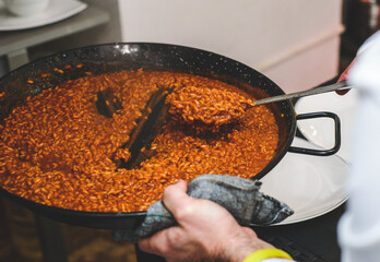 Camarero sirviendo una paella de marisco gourmet con langostinos y calamares en un restaurante de...