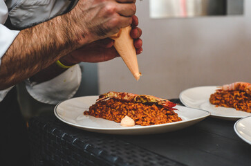 Camarero sirviendo una paella de marisco gourmet con langostinos y calamares en un restaurante de...