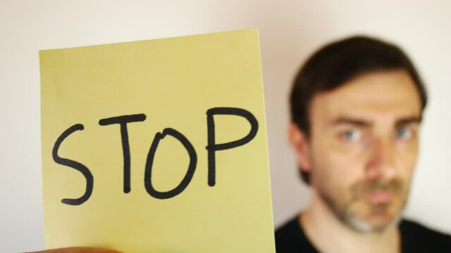 Blurred caucasian man showing a sticker with the writing "stop". Useful to illustrate several topics, such as war, racism, discrimination, terrorism, social issues, idealism, pollution, climate change