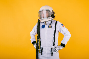 Male cosmonaut in space suit and helmet with foggy glass, arms at waist, on yellow background.