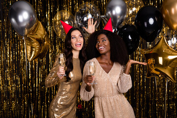 Photo of two glamour stunning ladies hold champagne wear cone hat birthday balloons isolated on shine bright tinsel background