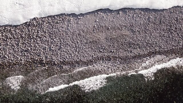 winter aerial flight top over waves rolling on artic ocean shore with round stones, ocean waves at storm