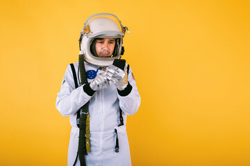 Male cosmonaut in space suit and helmet, talking on the mobile phone, on yellow background. © Davidbenito