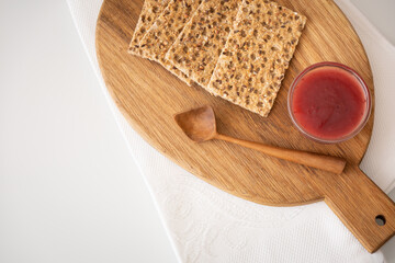 Strawberry jam, organic crispbread and a wooden spoon on a cutting board. Wooden cutting board with delicious healthy snack. Healthy eating concept