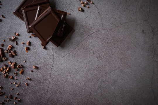 Pieces of dark chocolate with raw cacao nibs on grey stone background. High quality chocolate bar treat. Side border from top view. Empty space for text. Copy space. 