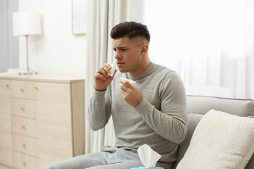 Ill man with paper tissue using nasal spray at home