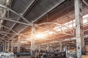 Old abandoned decay industry factory or plant building interior with concrete and steel metal construction frame beams. Sunlight warm sun through rooftop window. Dark grungy industrial background