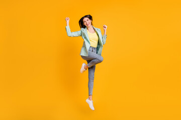 Fototapeta na wymiar Full length photo of charming lucky young woman wear teal blazer jumping rising fists isolated yellow color background