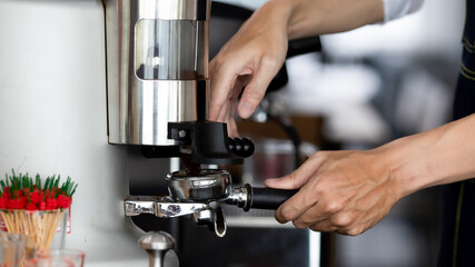 close up photo of male hands holding a metal tamper and a portafilter with coffee in a coffee shop. A man barista preparing for pressing ground coffee for brewing espresso or americano in a cafe.