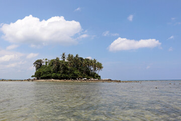 Tropical island with coconut palm trees in a ocean, picturesque view from the water. Colorful seascape with blue sky and white clouds, concept of travel and vacation on paradise nature