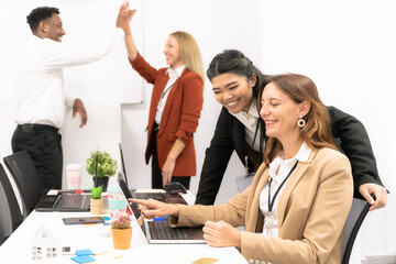Group of multiracial business people working and communicating while sitting at the office desk together with colleagues high fiving in the background. Happy teacher explaining the lesson.