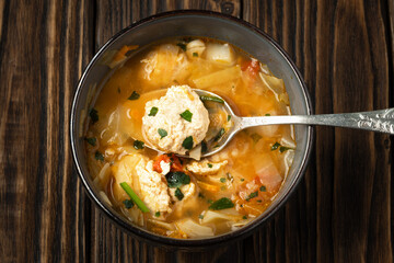 Close up of a soup with chicken meatballs and on the dark brown wooden boards