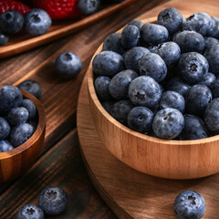 Bamboo cup with ripe fresh blueberries on a wooden stand surrounded by berries. Square. Close-up